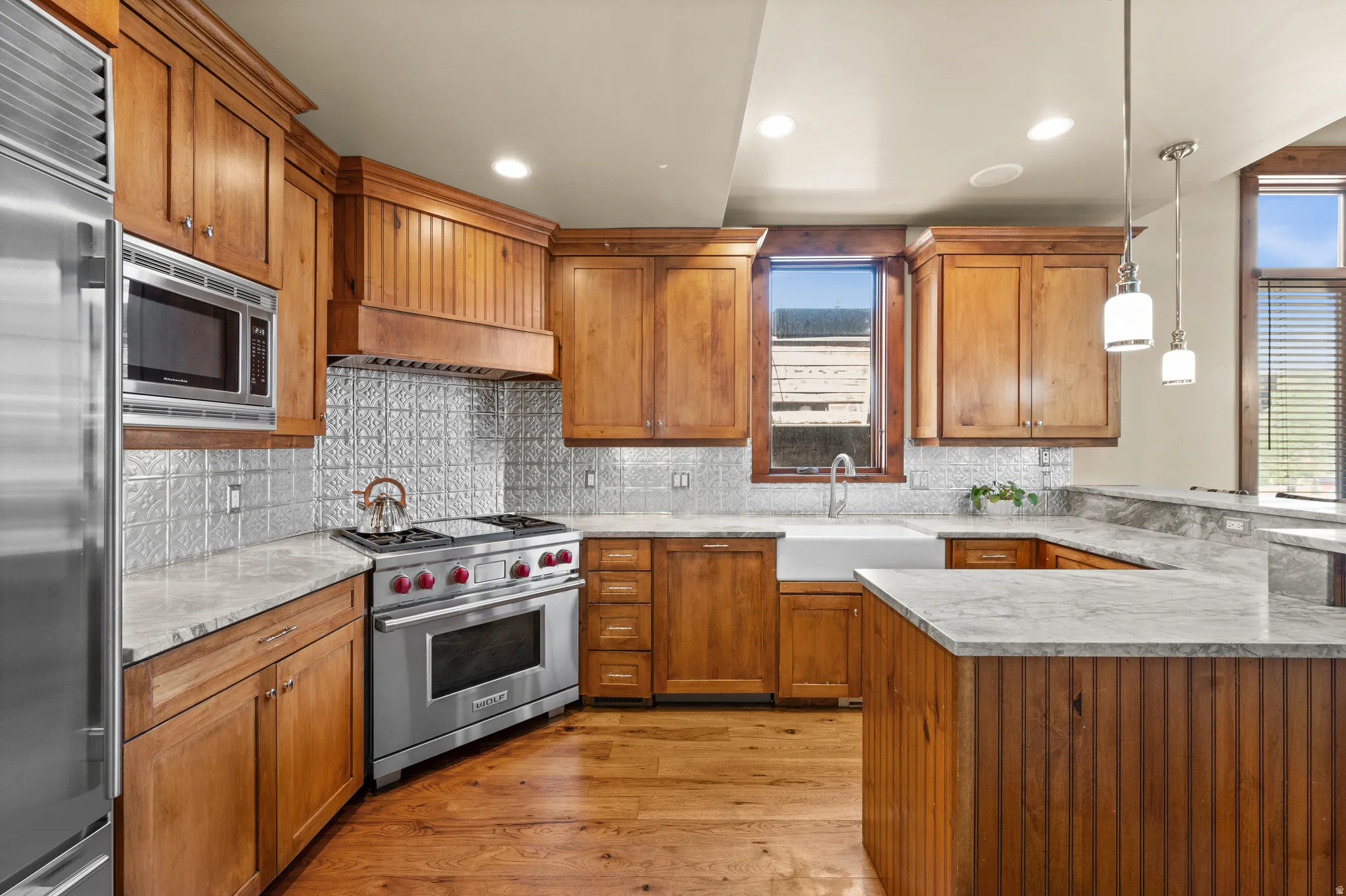 Kitchen featuring light wood cabinetry, light-toned countertops, a white farmhouse sink, stainless steel appliances, and a pressed tin backsplash
