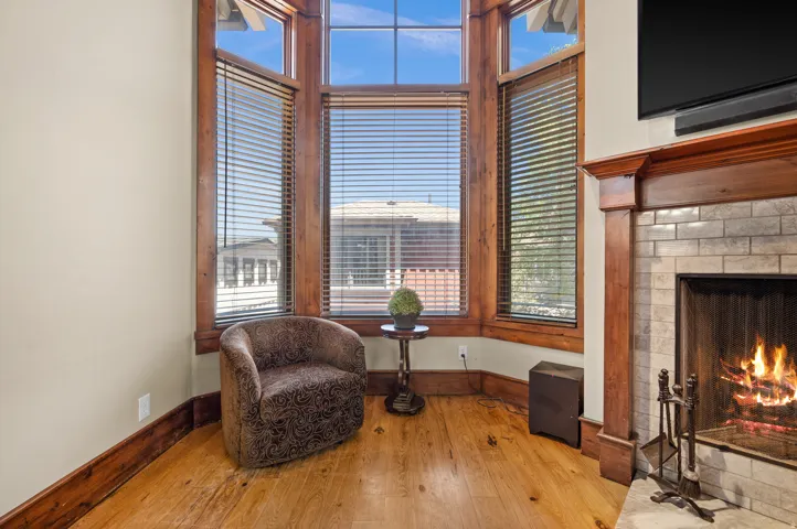 Bay window with wood-finish trim, wood-finish flooring, and a fireplace with a light-colored brick surround