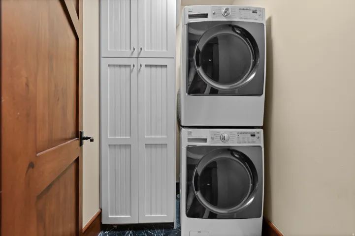 Laundry area featuring a stackable washer and dryer, beadboard cabinetry, a wooden door with dark hardware, and dark flooring