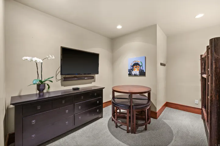 Wall-mounted television with soundbar, built-in dresser with multiple drawers, light-colored carpeting, recessed lighting, and wood baseboards