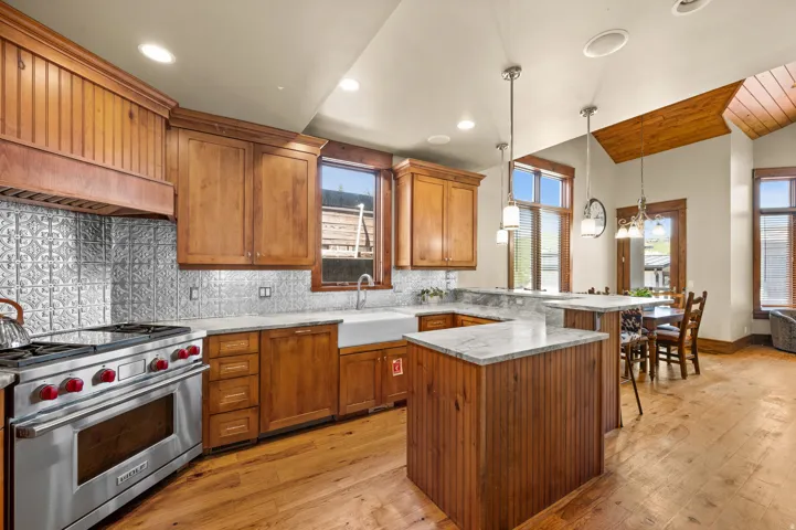 Gourmet kitchen featuring a stainless steel range with red knobs, wood cabinetry, a white farmhouse sink, and marble-finish countertops