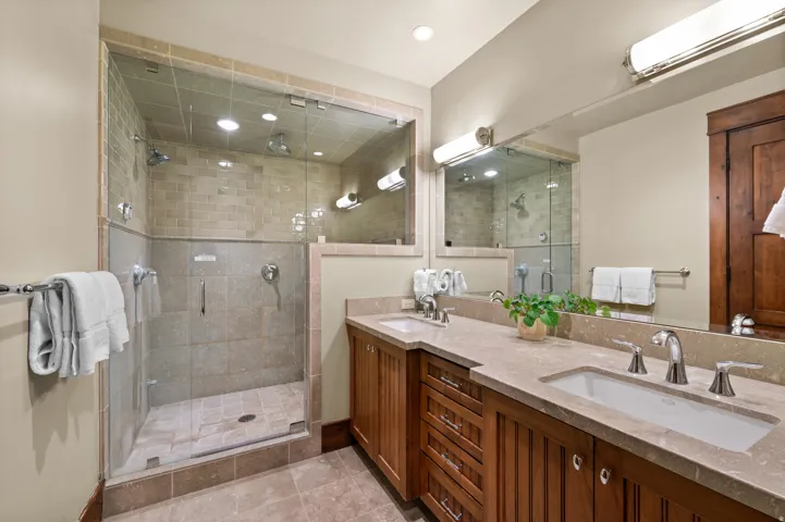 Bathroom featuring a glass-enclosed shower with multiple showerheads, dual vanity with undermount sinks, and a stone countertop