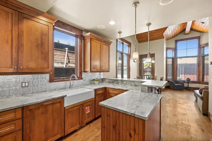 Kitchen featuring wood cabinetry, an apron-front sink, pressed metal tile backsplash, and light-toned countertops