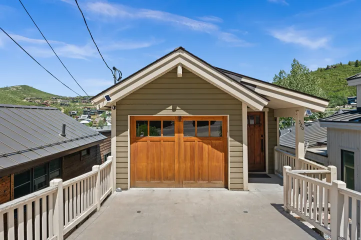 Property exterior featuring light green siding and a prominent wood-finish garage door with upper window inserts