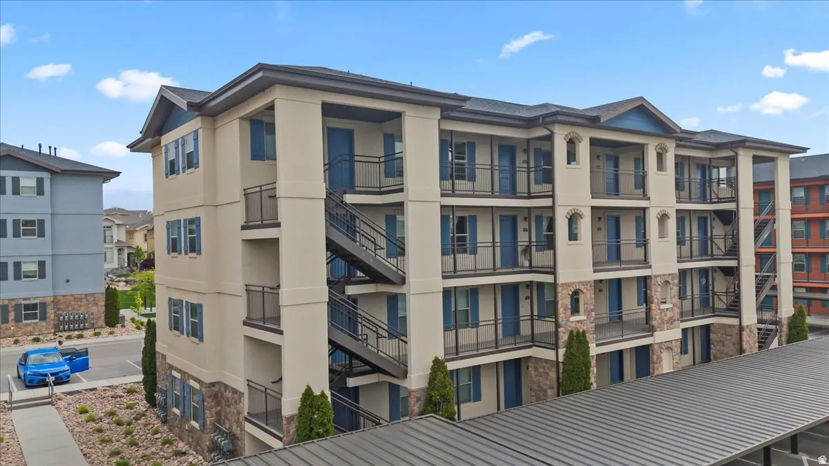Multi-story building featuring a stucco and stone veneer exterior, multiple balconies with black railings, exterior staircases, and blue accent shutters and doors
