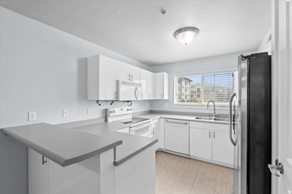 Modern kitchen featuring white cabinetry, light countertops, wood-finish flooring, stainless steel appliances, and a breakfast bar