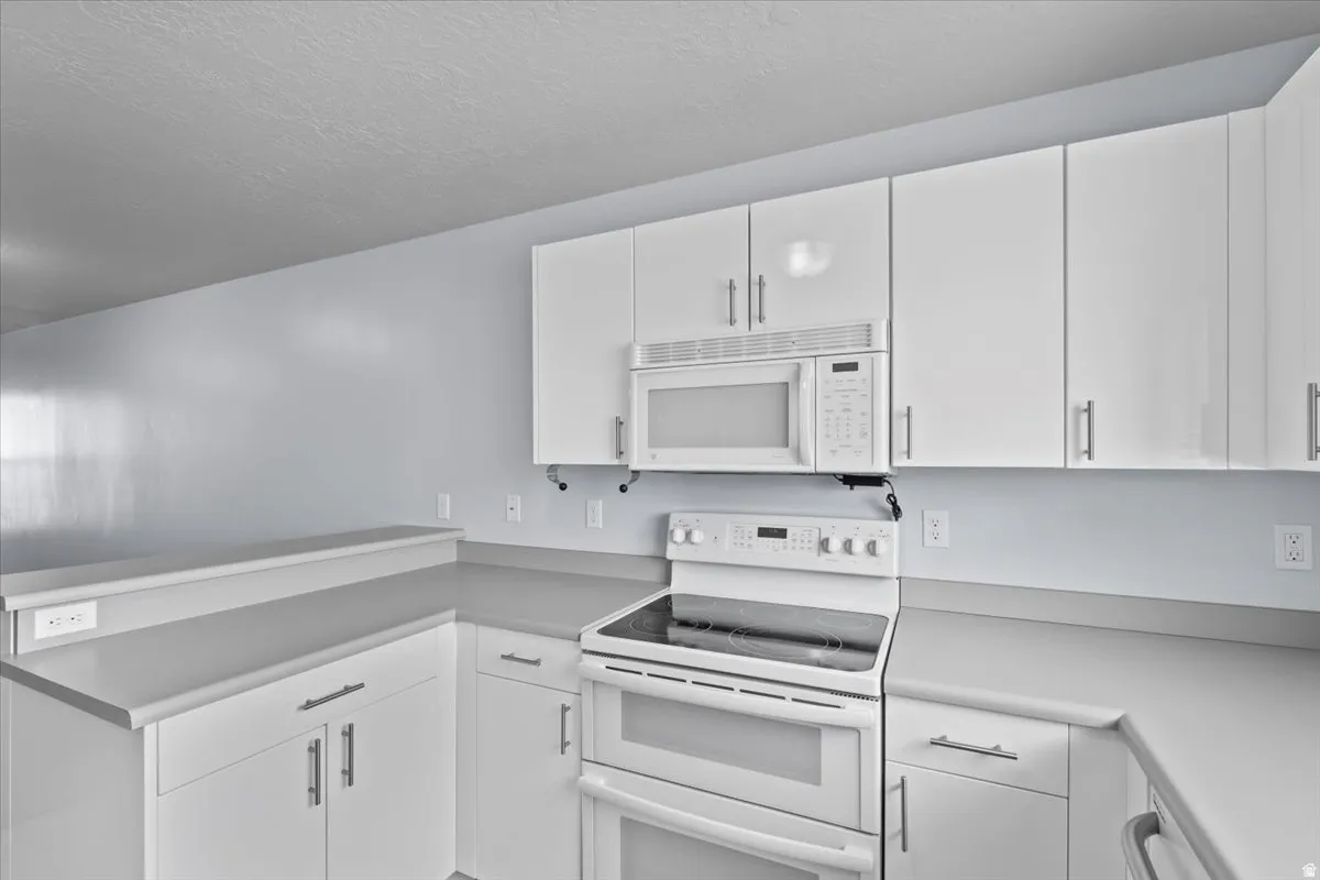Kitchen featuring white cabinetry, light gray countertops, white double oven range, white built-in microwave, and a breakfast bar