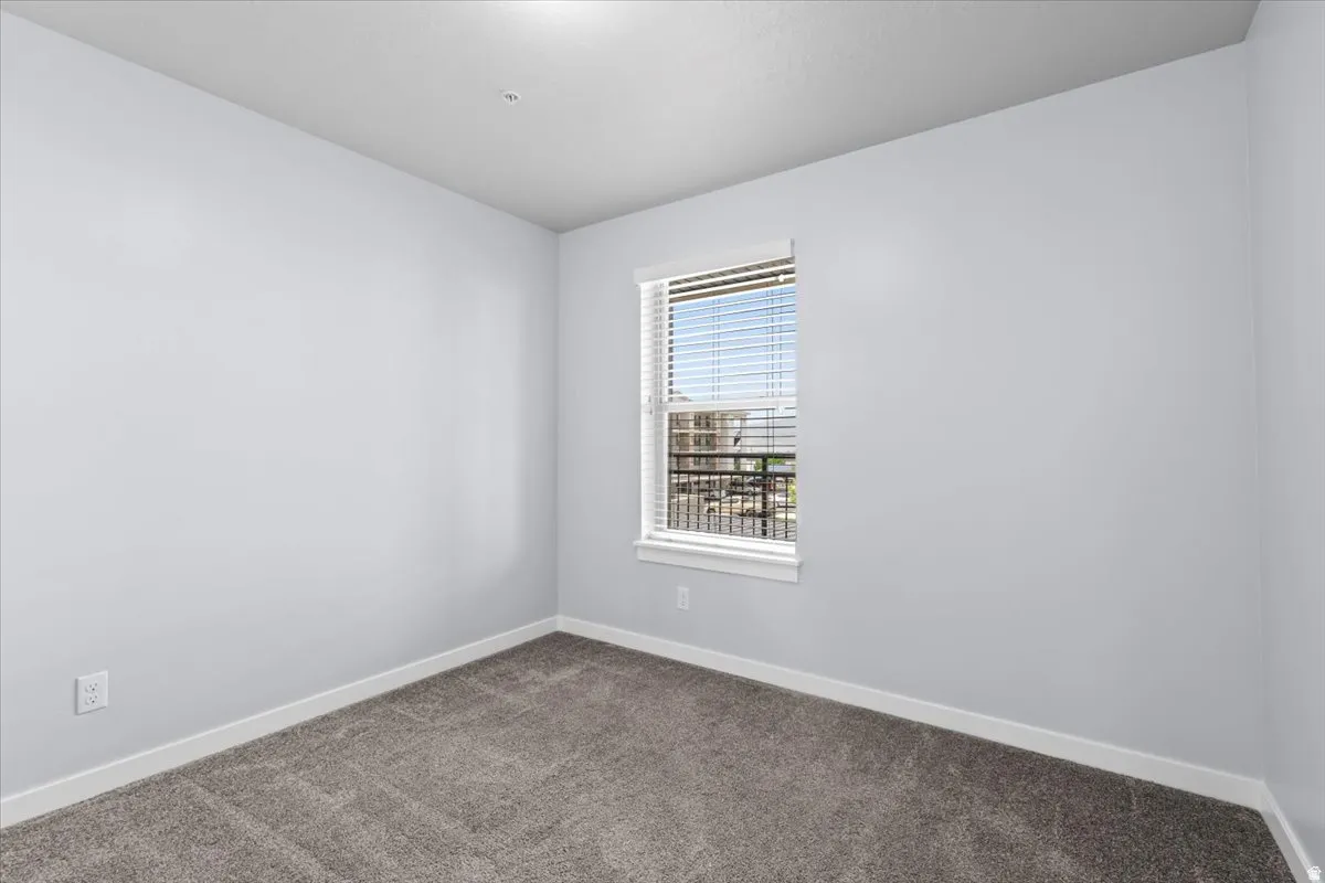 Interior room featuring neutral wall tones, gray carpeting, white baseboards, and a single window with blinds