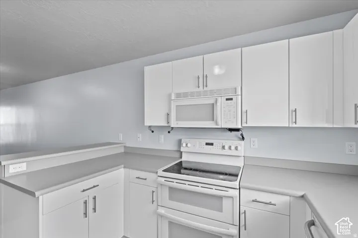 Kitchen featuring white cabinetry, light gray countertops, white double oven range, white built-in microwave, and a breakfast bar