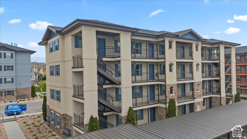 Multi-story building featuring a stucco and stone veneer exterior, multiple balconies with black railings, exterior staircases, and blue accent shutters and doors