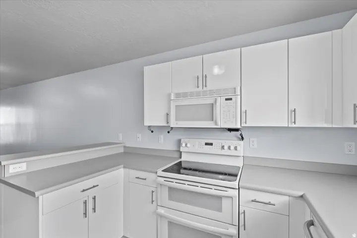 Kitchen featuring white cabinetry, light gray countertops, white double oven range, white built-in microwave, and a breakfast bar