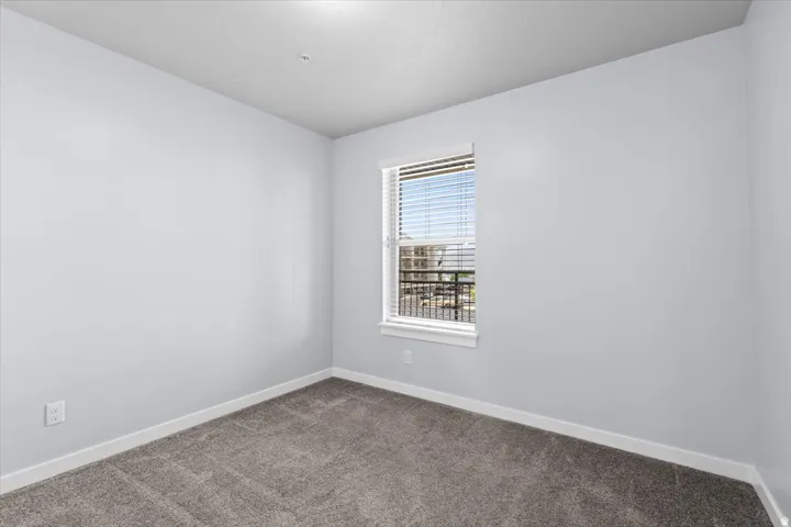 Interior room featuring neutral wall tones, gray carpeting, white baseboards, and a single window with blinds