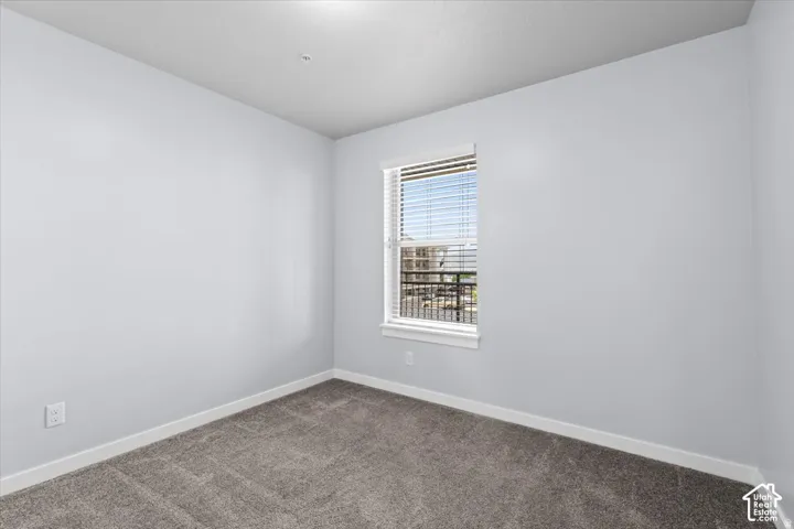 Interior room featuring neutral wall tones, gray carpeting, white baseboards, and a single window with blinds