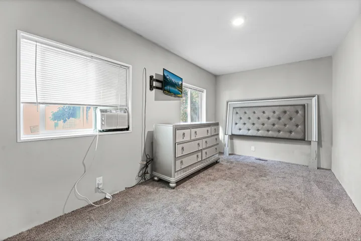 Neutral-toned room featuring a single window with blinds and a window-mounted air conditioning unit