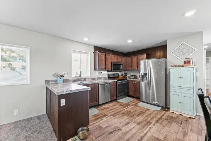 Open-concept kitchen featuring wood-finish flooring, dark wood cabinetry, light-toned countertops, and stainless steel appliances