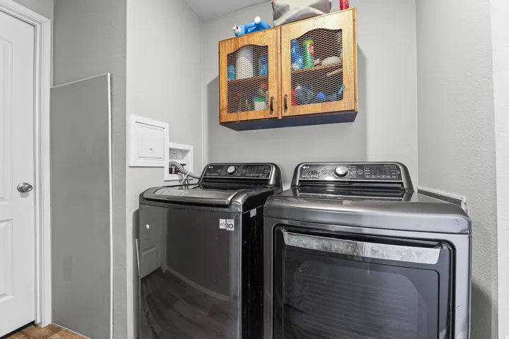 Dedicated laundry area featuring a white door, light gray walls, wood-finish flooring, and wall-mounted wooden cabinetry with mesh inserts