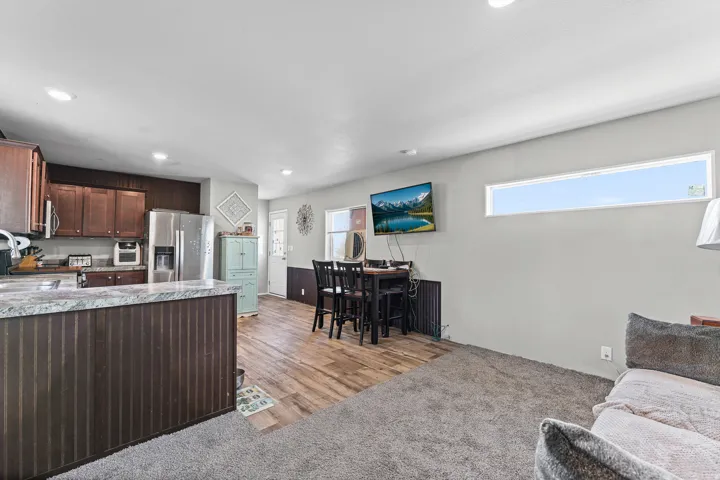 Open-concept living area featuring distinct flooring zones with wood-finish flooring and carpeting, a breakfast bar with beadboard paneling, recessed lighting, and a horizontal window