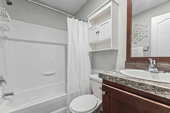 Bathroom featuring a white tub and shower combination, a white toilet, a wood-finish vanity with a built-in sink, and a granite-patterned countertop