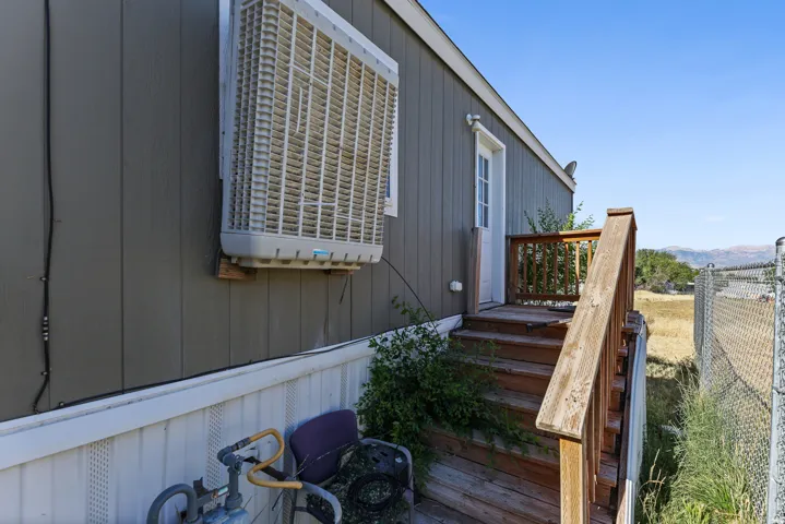Exterior featuring vertical panel siding, a side door, a wooden deck with railings, and an exterior cooling unit