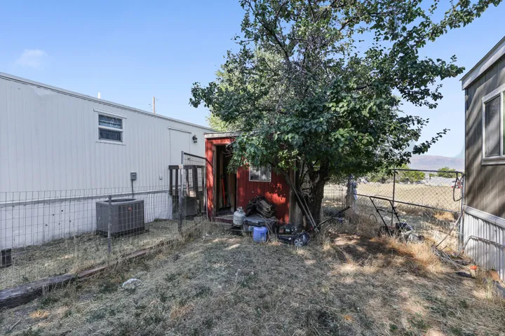 White corrugated siding exterior with a dark red entryway and a mature tree