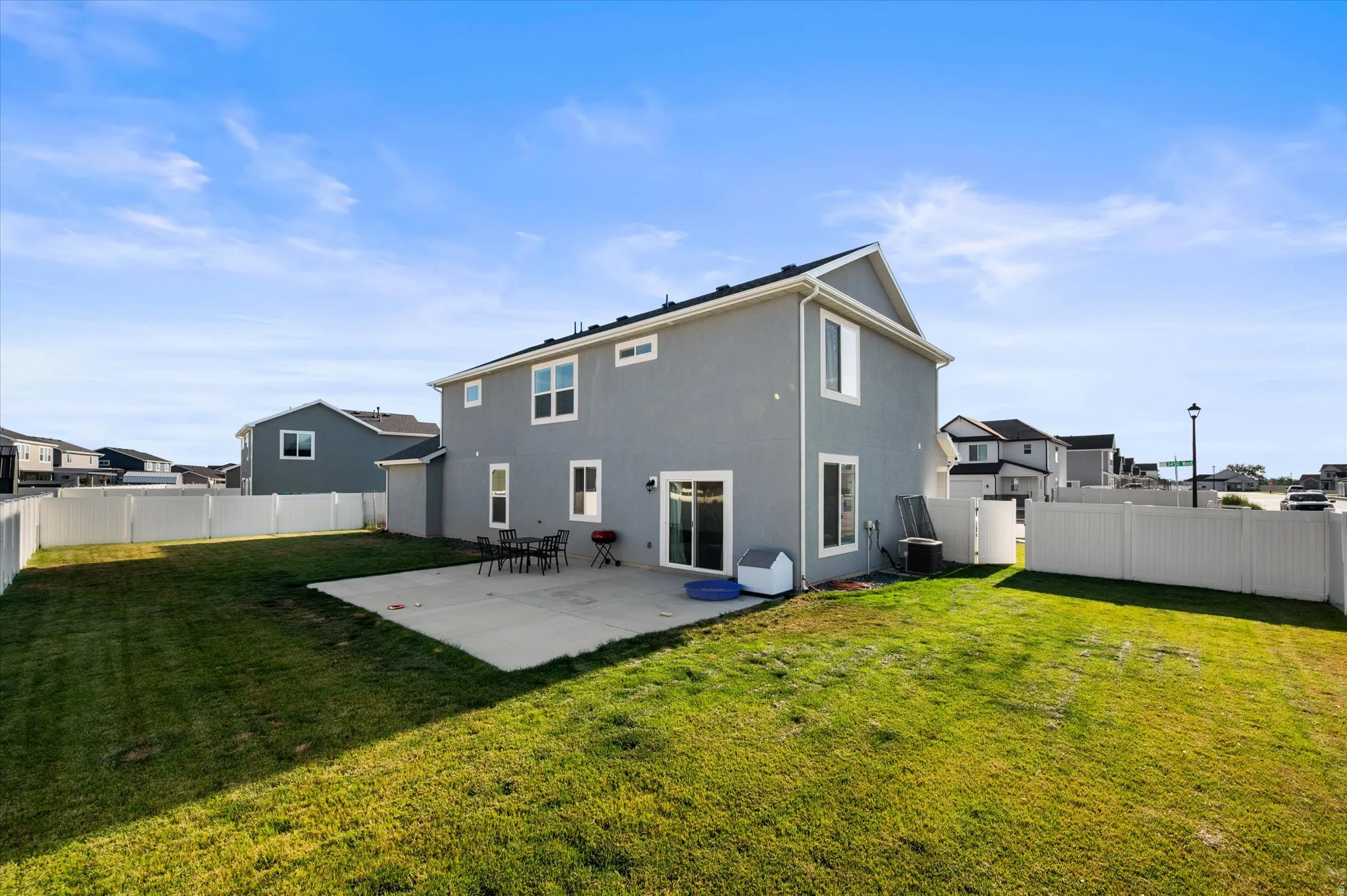 Expansive backyard featuring a concrete patio, white perimeter fencing, and a manicured lawn