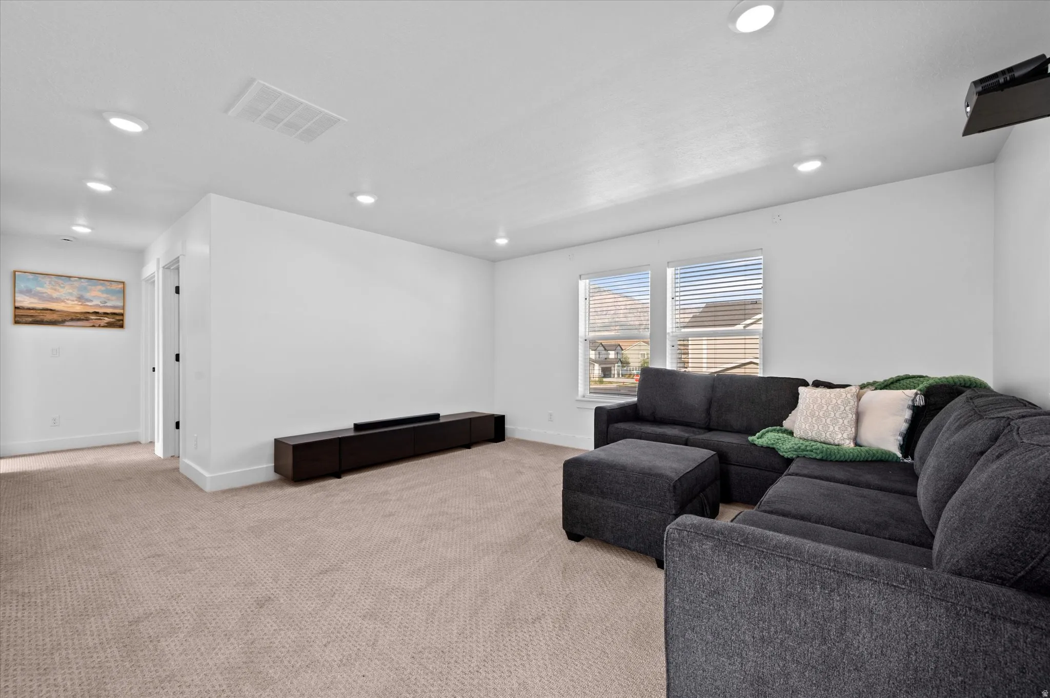 Recessed lighting, neutral carpeting, two windows with blinds, and white walls