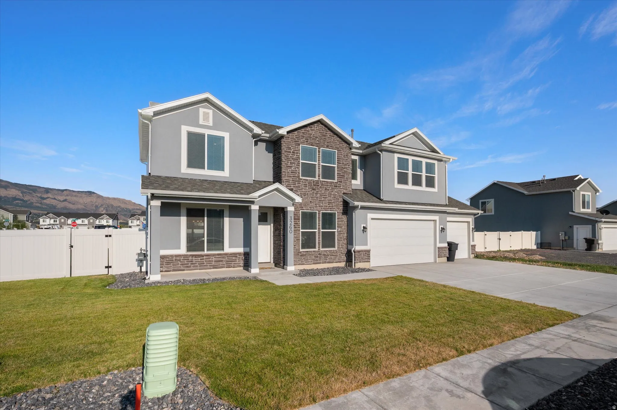 Two-story residence featuring a gray and stone facade, attached two-car garage, and a concrete driveway