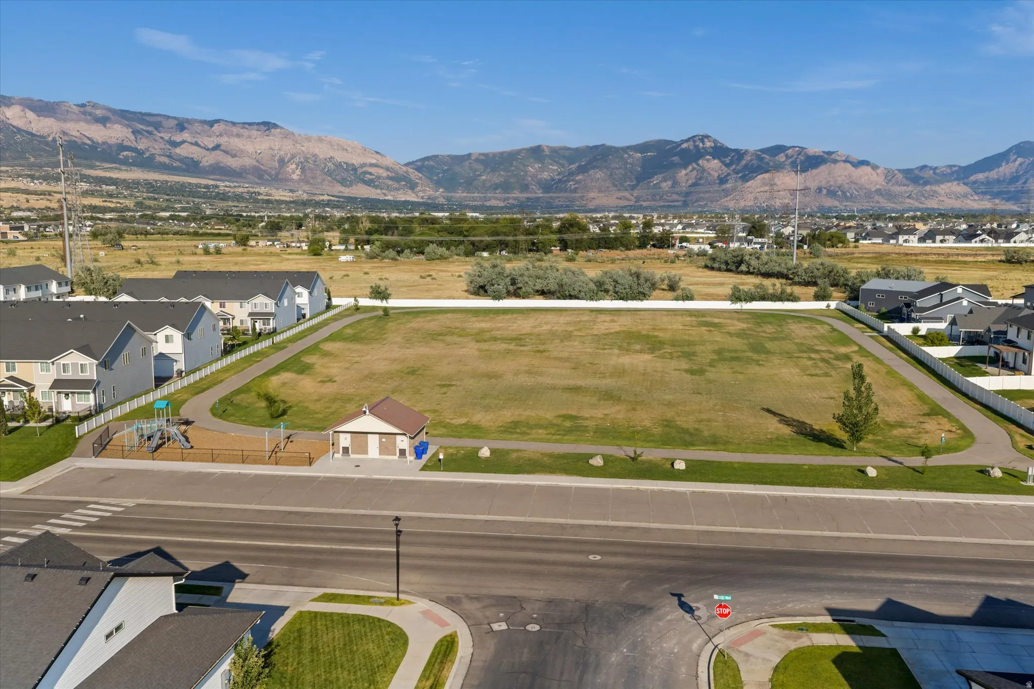 Expansive green space bordered by paved pathways, surrounded by residential properties, with distant mountains providing a scenic backdrop