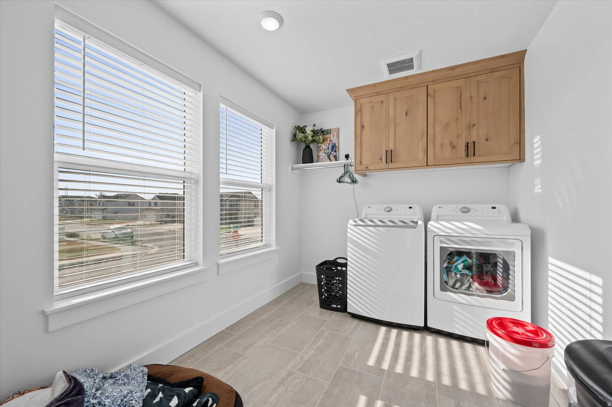 Laundry space featuring a mounted wooden cabinet, two windows with blinds, recessed ceiling lighting, and tiled flooring