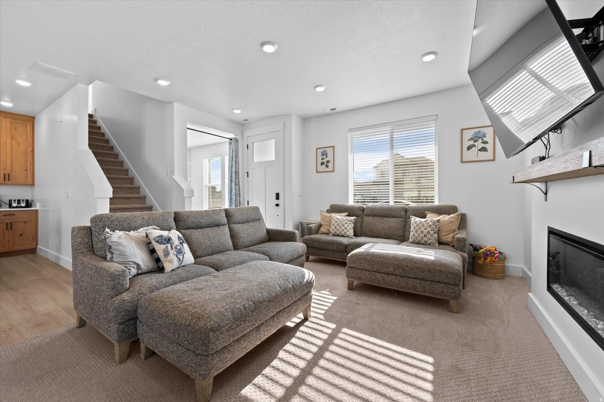 Open-concept living area featuring an integrated fireplace, recessed lighting, large windows, and a built-in staircase