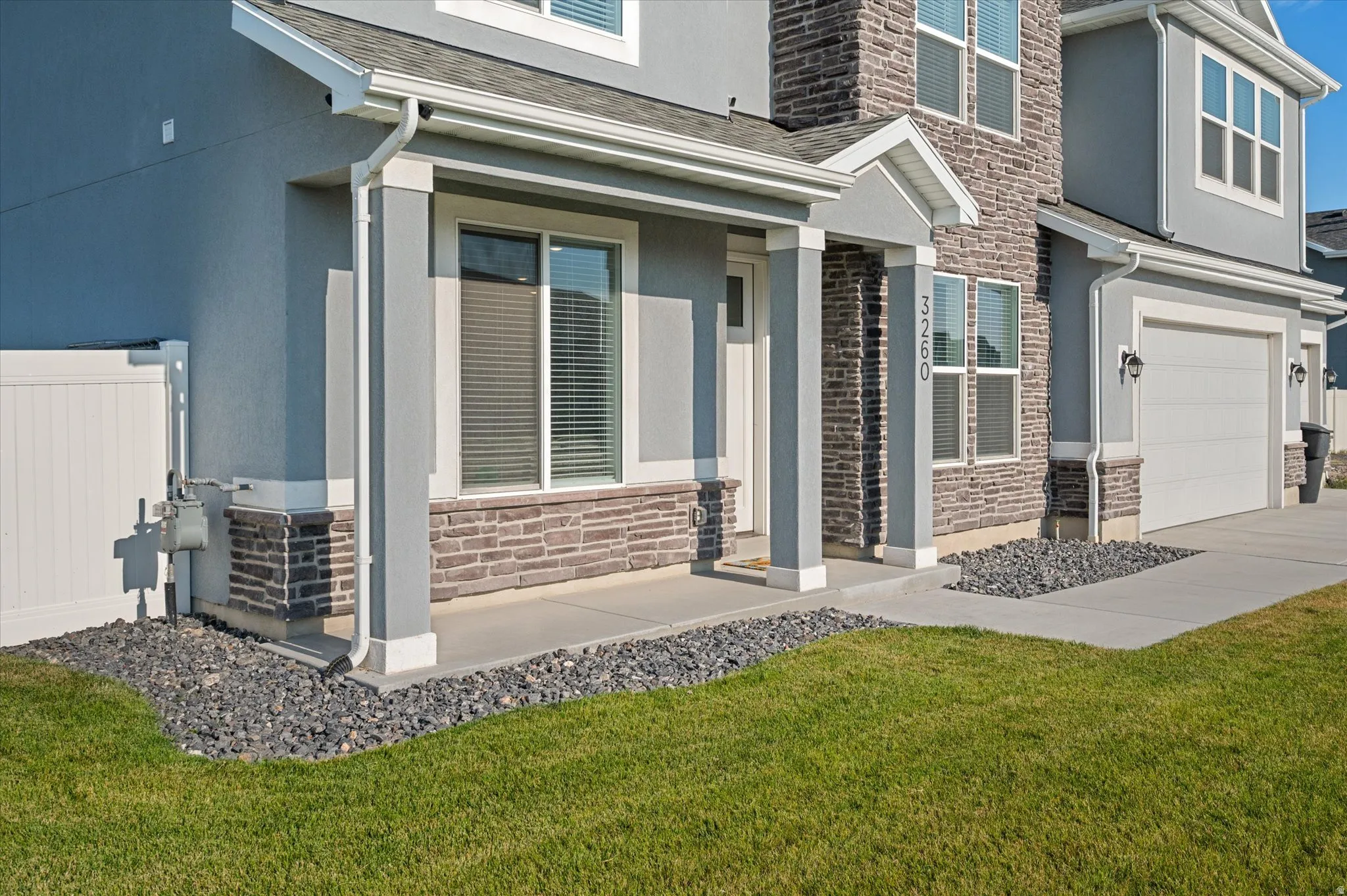 Exterior featuring a stone and stucco facade, white garage door, and a concrete walkway bordered by decorative rock