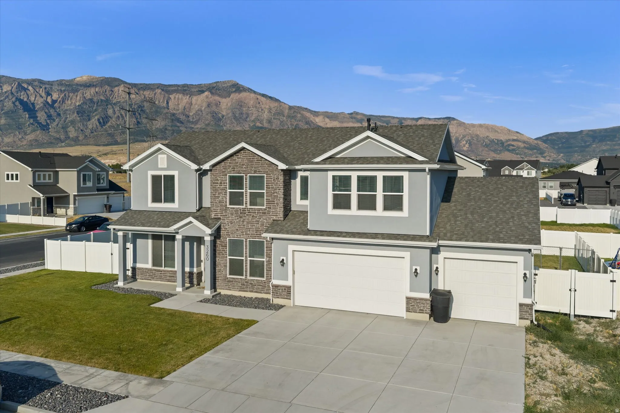 Two-story residence featuring a combination of stucco and stone exterior finishes, a covered porch entry, and a multi-car garage with overhead doors