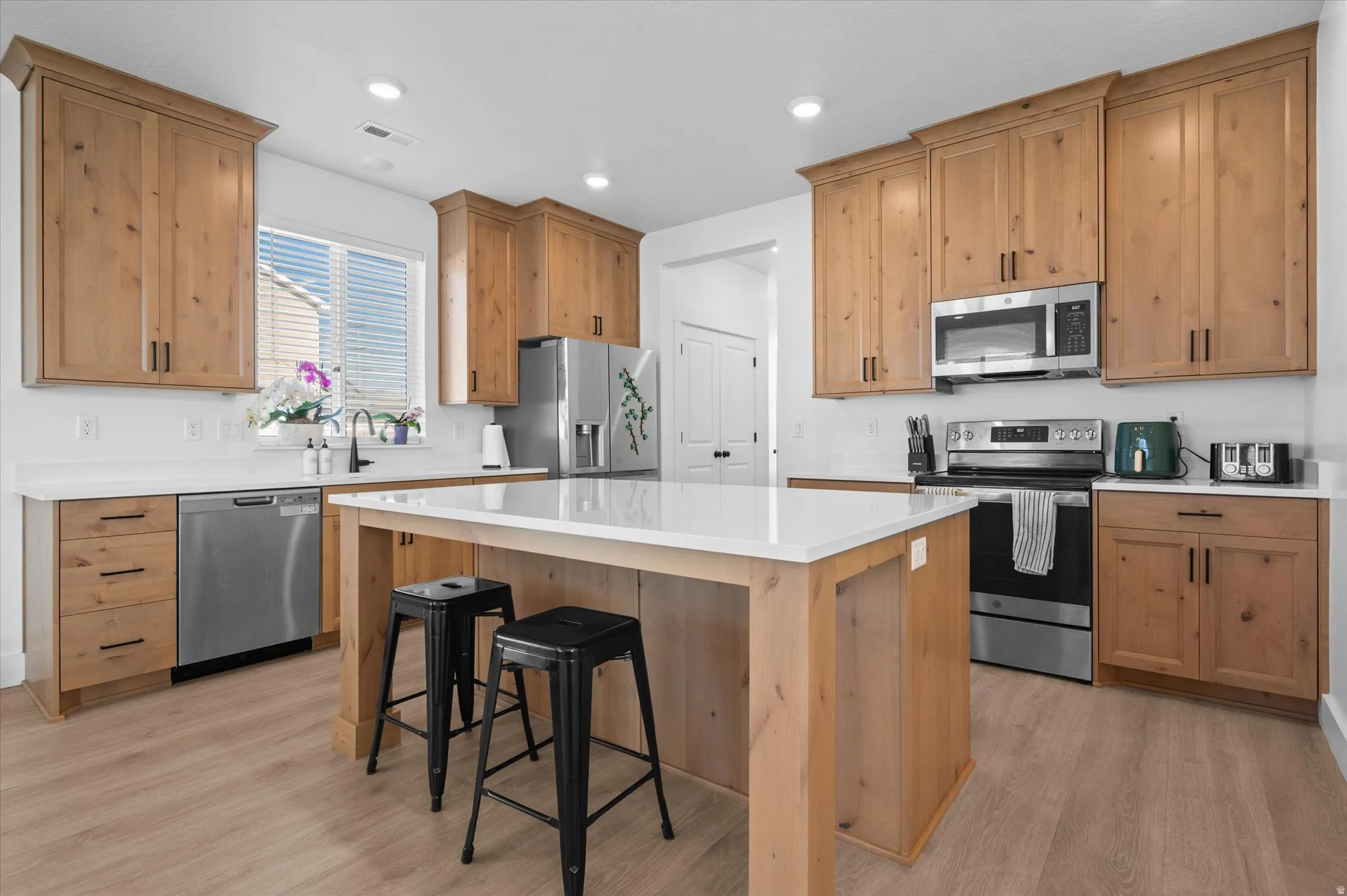 Kitchen featuring wood-finish cabinetry, stainless steel appliances, a center island with counter seating, white countertops, and wood-finish flooring