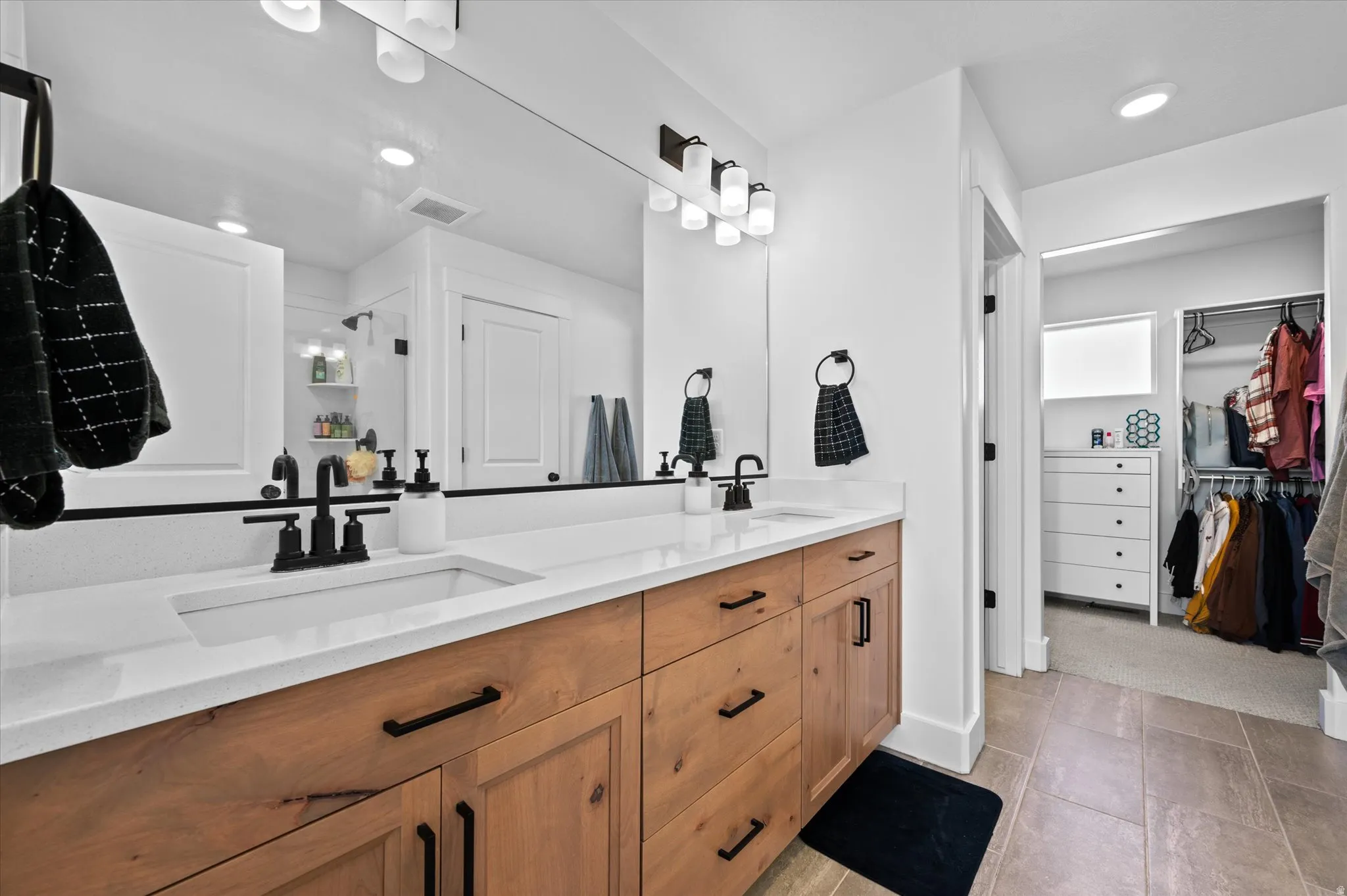 Dual vanity with wood-finish cabinetry, white countertops, and matte black fixtures