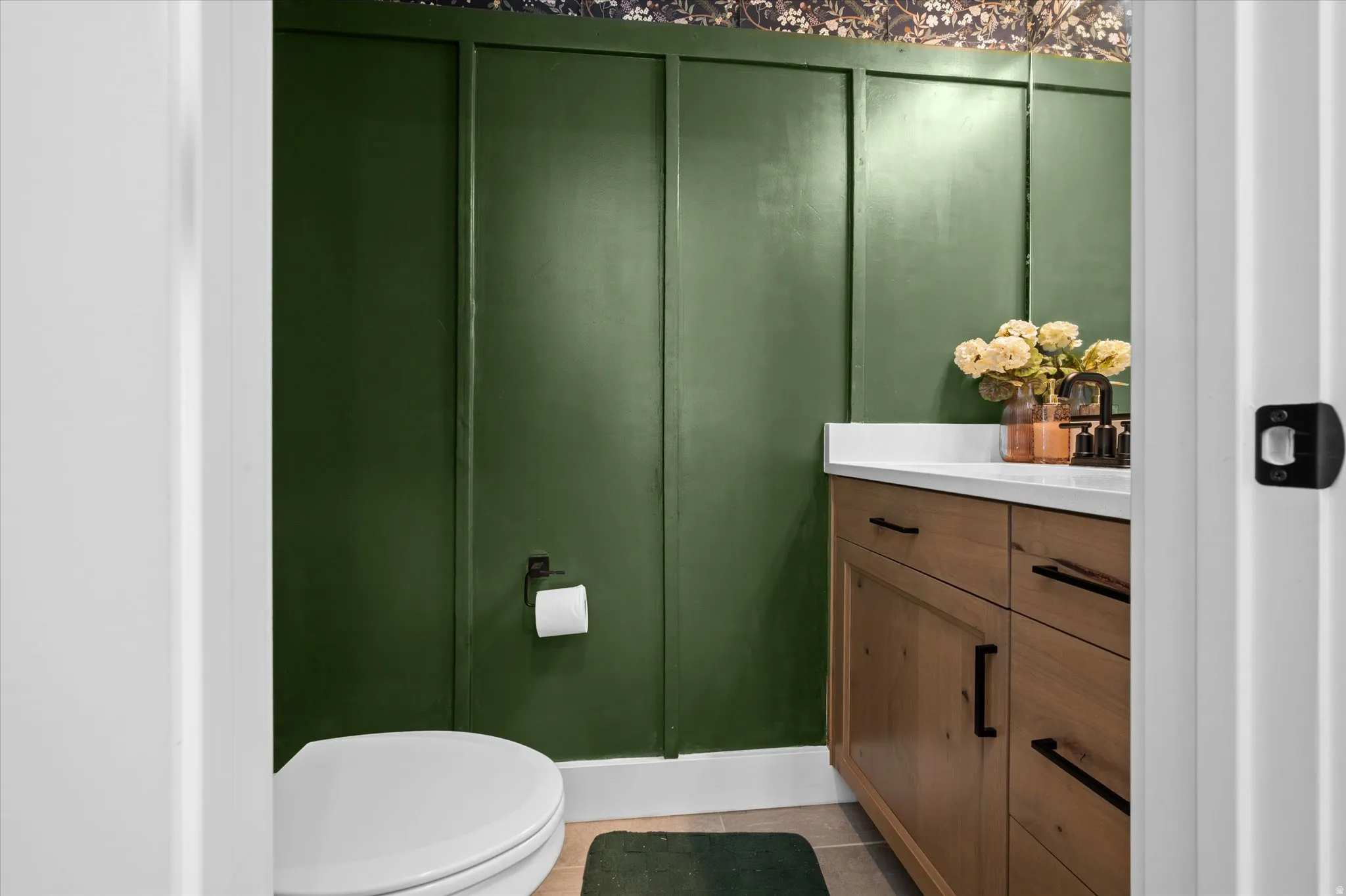 Wood-finish vanity with a white countertop and dark hardware, complemented by a green board and batten wall treatment