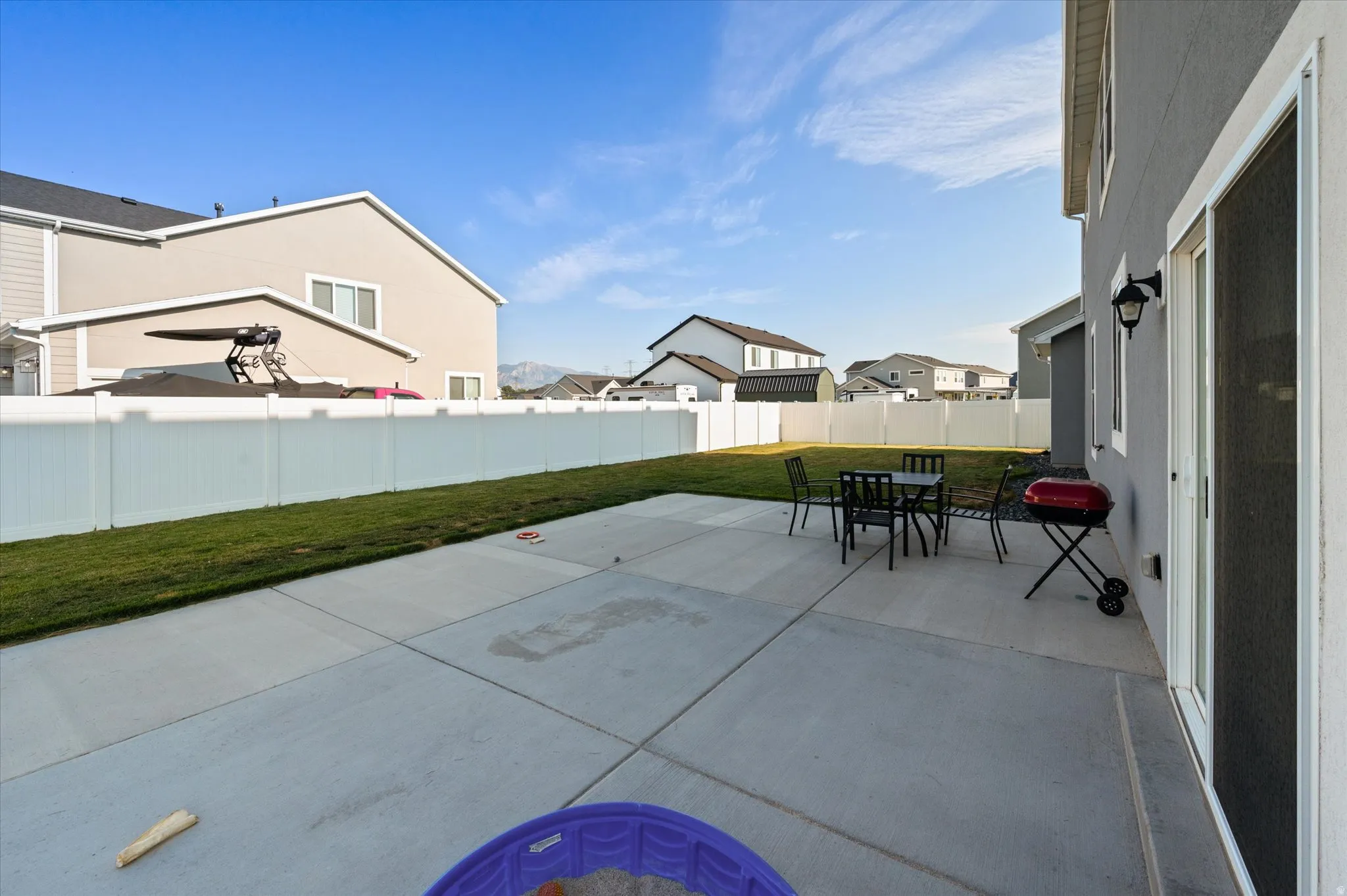 Concrete patio with a sliding glass door, exterior wall lantern, and a white privacy fence