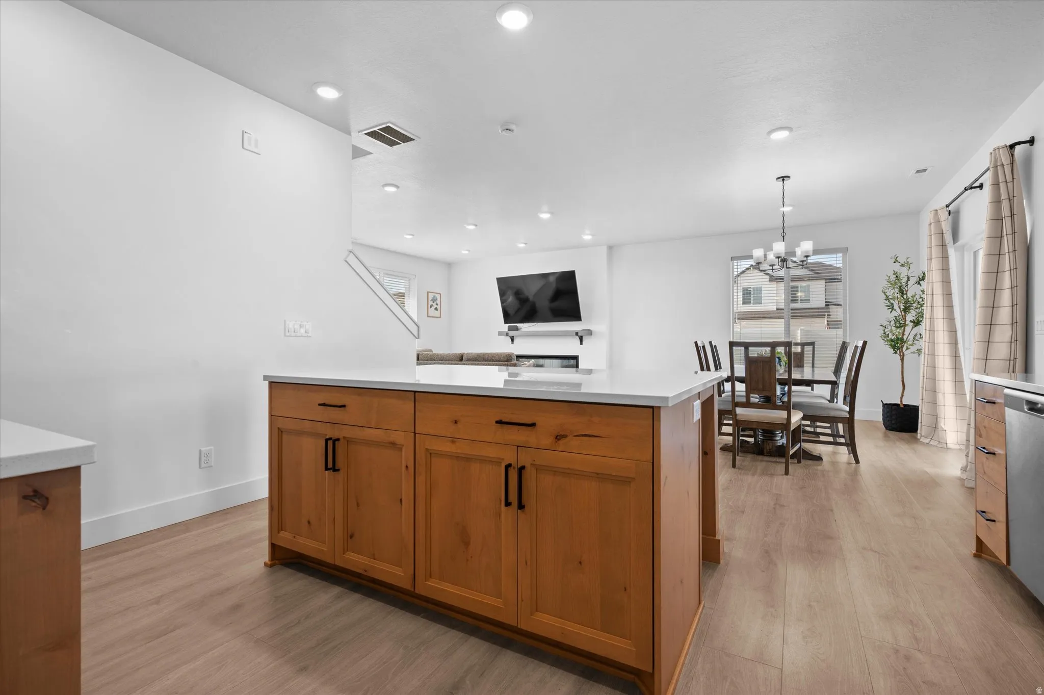 Kitchen island with a white countertop and wood-finish cabinetry, recessed lighting, wood-finish flooring, and a dining area with a chandelier