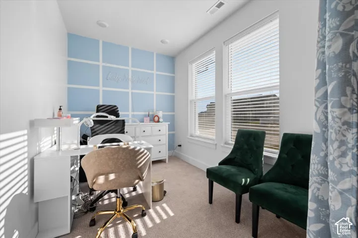 Recessed lighting, two bright windows with blinds, light wall-to-wall carpeting, and a decorative accent wall with grid paneling