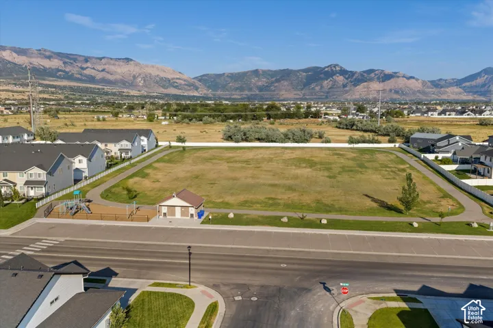 Expansive green space bordered by paved pathways, surrounded by residential properties, with distant mountains providing a scenic backdrop
