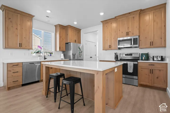 Kitchen featuring wood-finish cabinetry, stainless steel appliances, a center island with counter seating, white quartz countertops, and wood-finish flooring