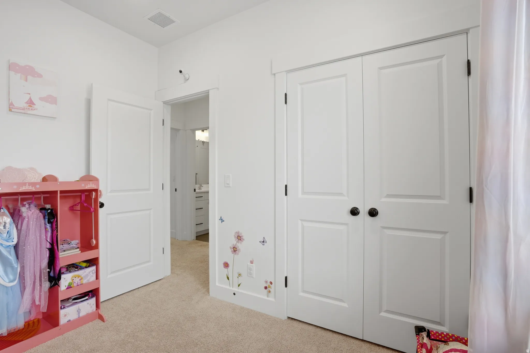 White interior with plush carpet flooring, showcasing a pair of paneled bifold closet doors with dark hardware