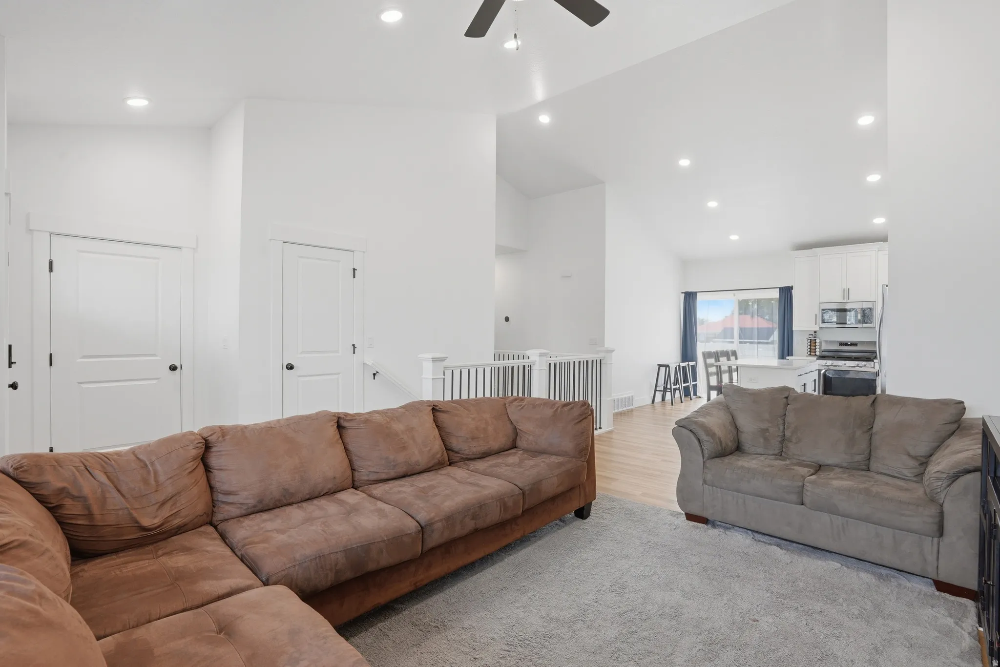 Open-concept living area featuring vaulted ceilings, recessed lighting, and light wood-finish flooring extending into the kitchen