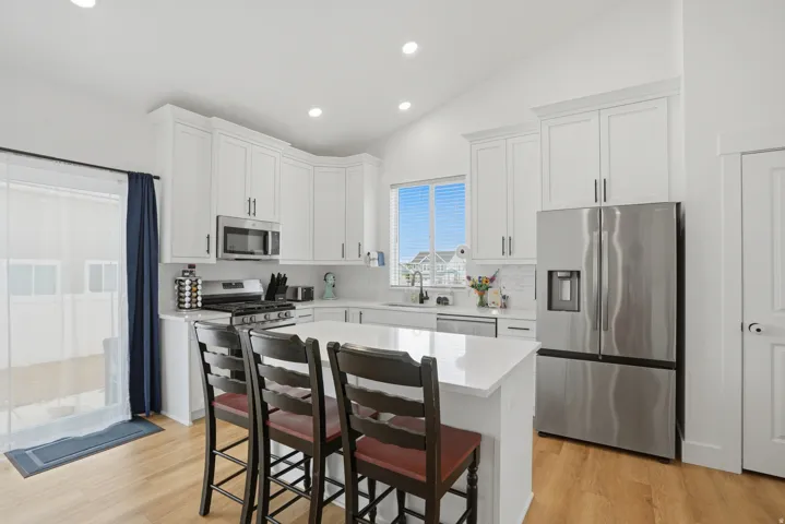 Modern kitchen featuring white cabinetry, stainless steel appliances, a center island with countertop seating, wood-finish flooring, and a sliding glass door