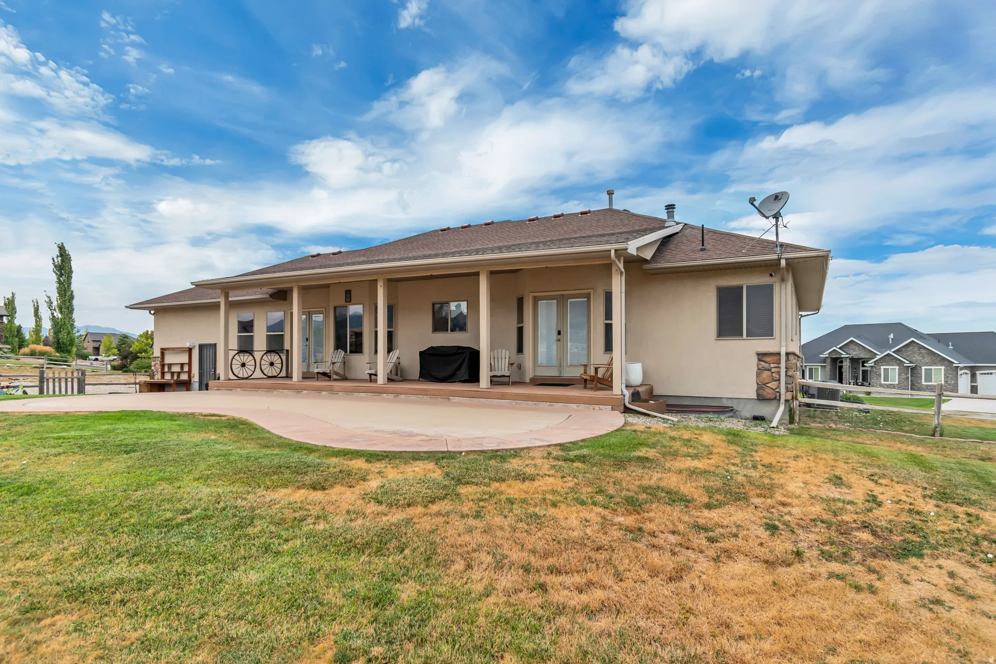 Expansive rear patio area featuring a covered porch, multiple entry points with glass-paneled doors, and a stone accent wall