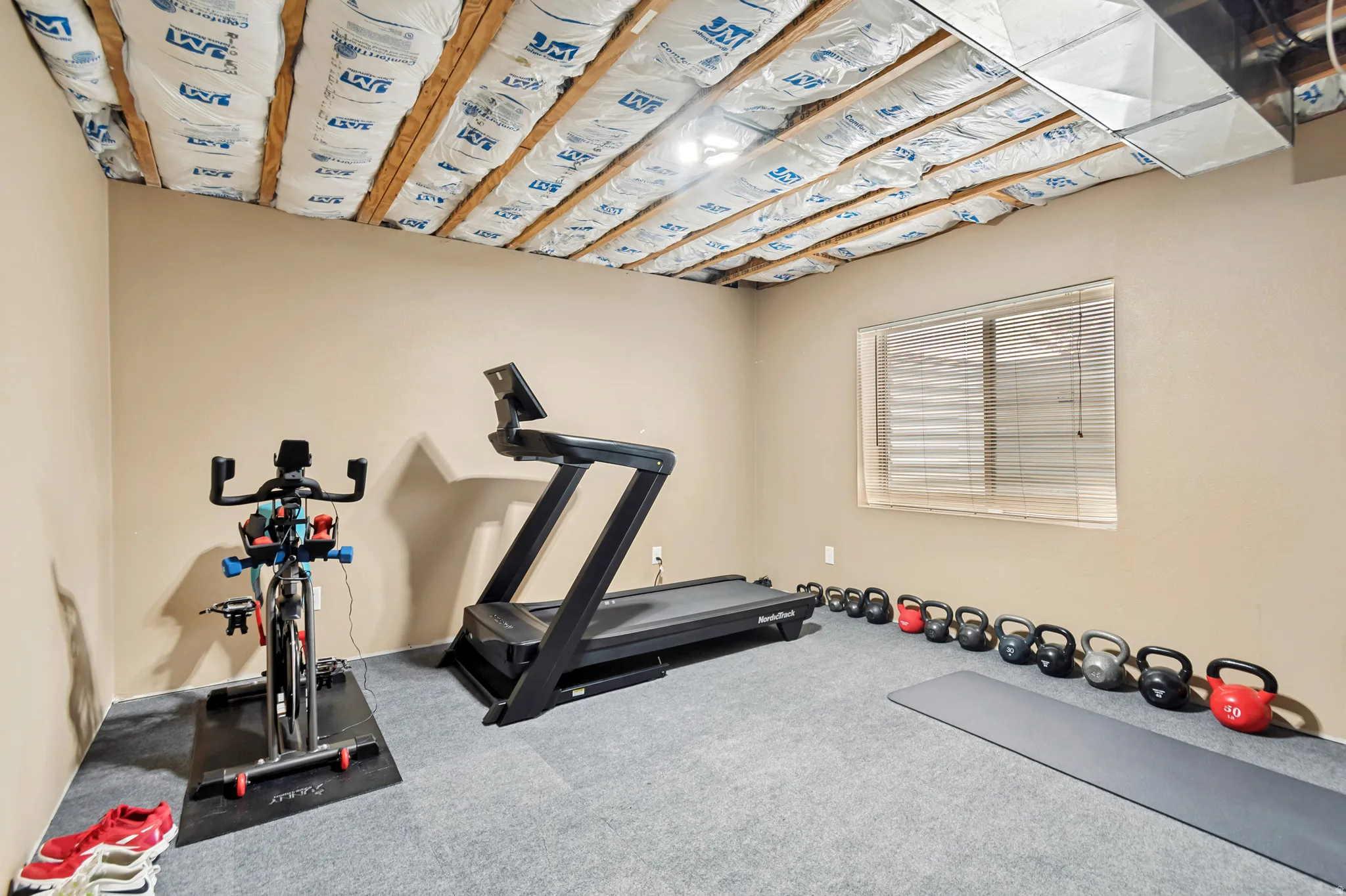 Spacious room with a neutral paint palette, light gray carpet flooring, and an exposed ceiling with visible insulation and ductwork