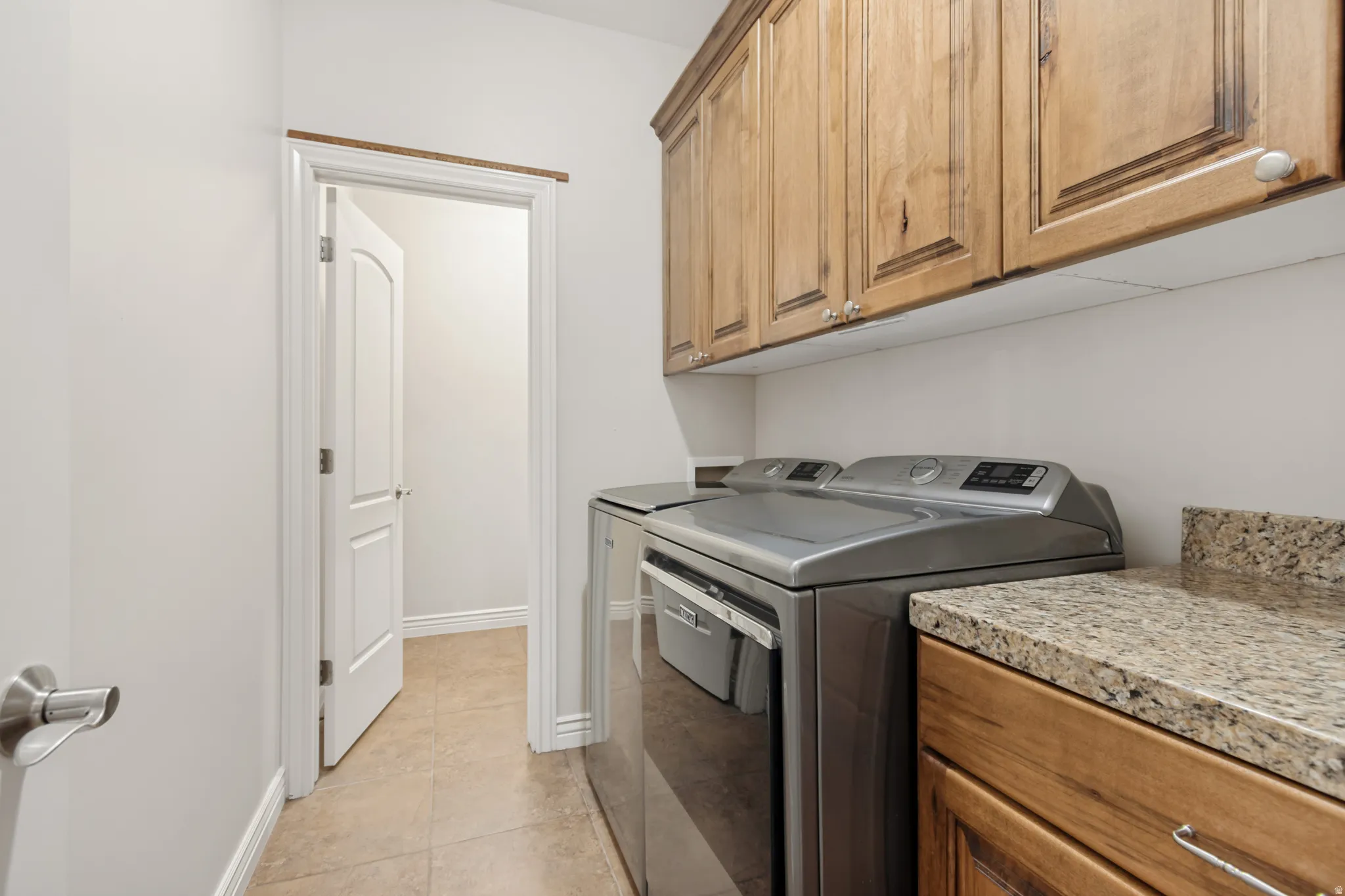 Laundry area featuring wood-finish cabinetry, granite-style countertop, and tile flooring