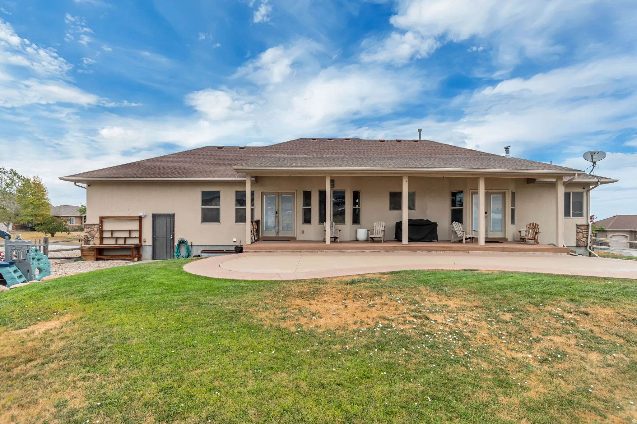 Rear stucco exterior with a covered porch and an expansive concrete patio