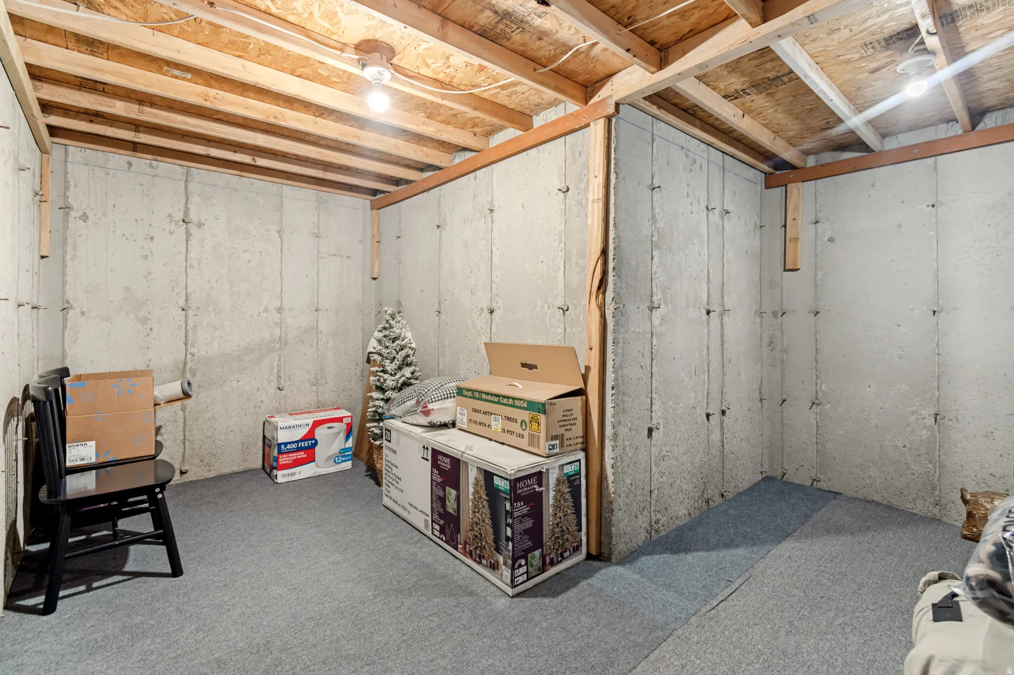 Unfinished basement area featuring concrete walls, exposed ceiling joists, and overhead lighting