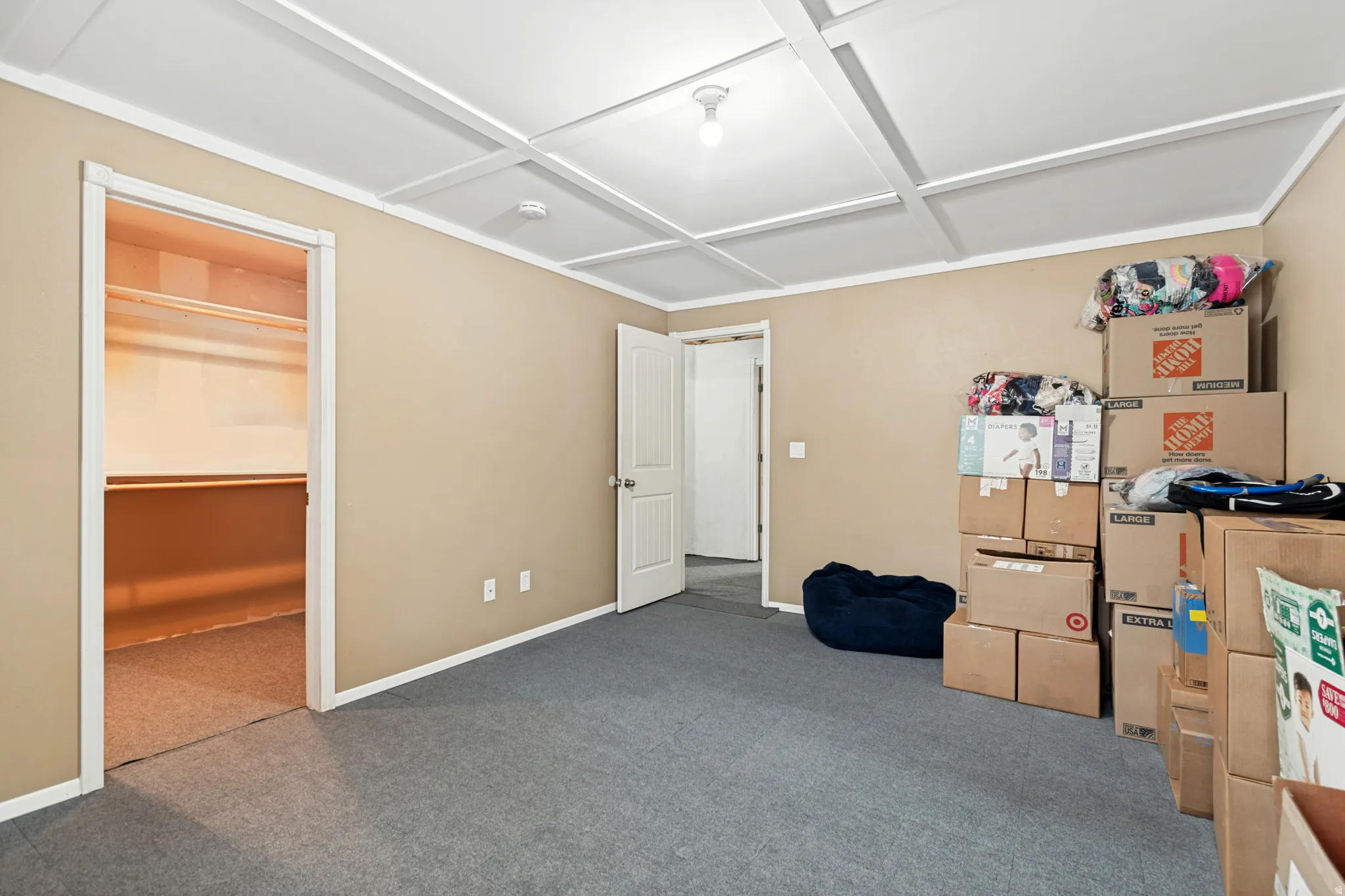 Carpeted room featuring a coffered ceiling, neutral wall tones, white trim, and a walk-in closet with shelving and hanging rods