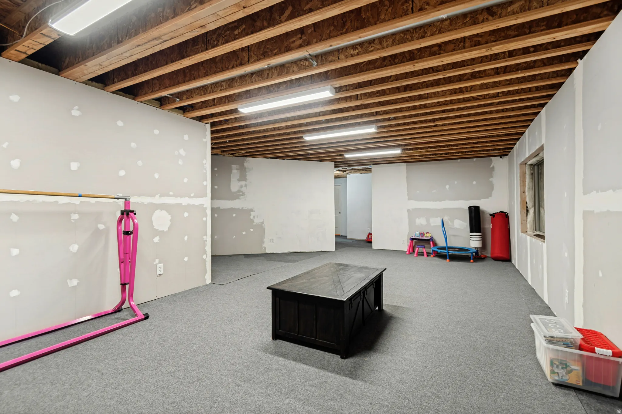 Expansive unfinished basement featuring exposed ceiling joists, drywall ready for finishing, and gray carpeting
